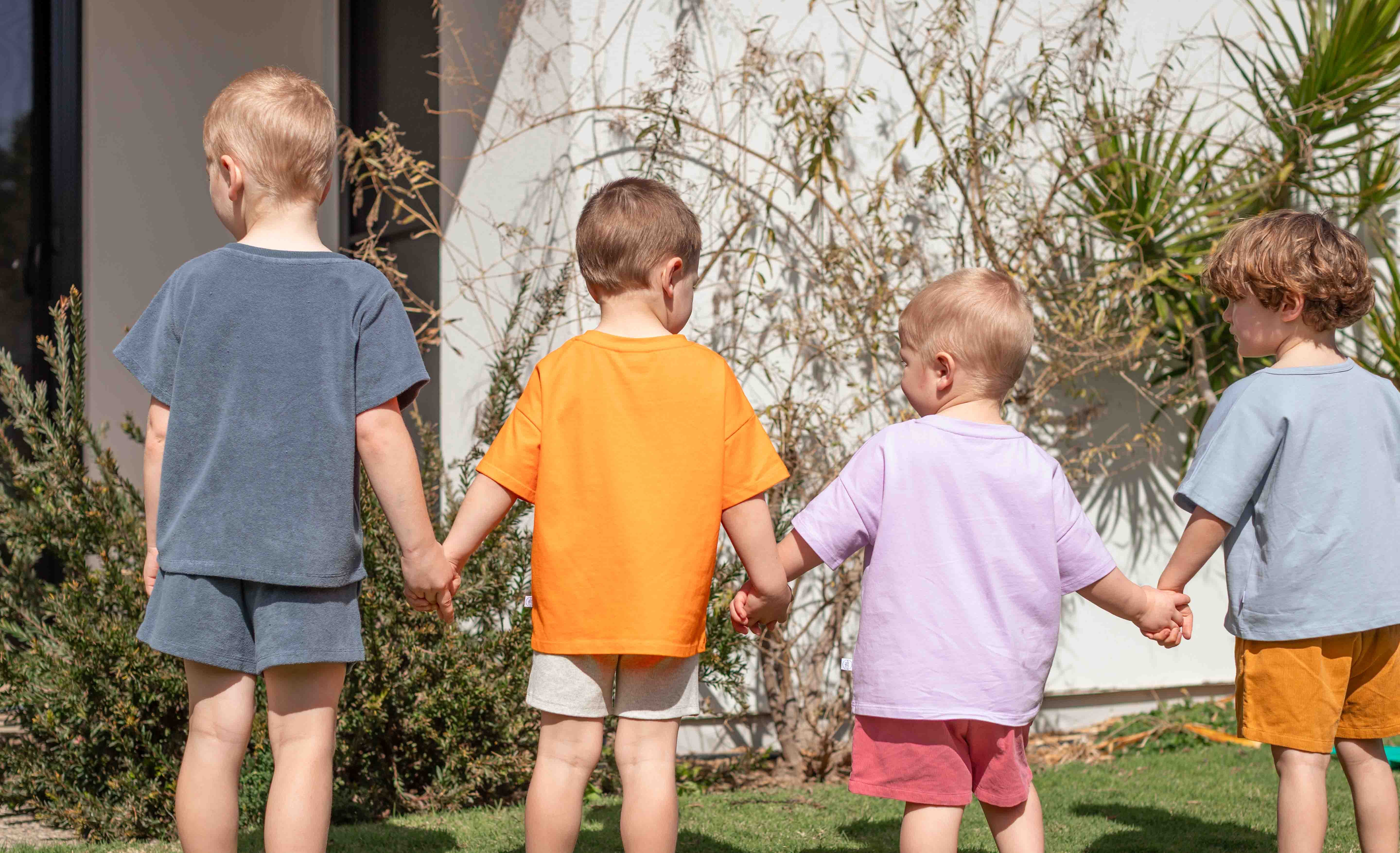 Four children holding hands in various brightly coloured t-shirts and short clothing