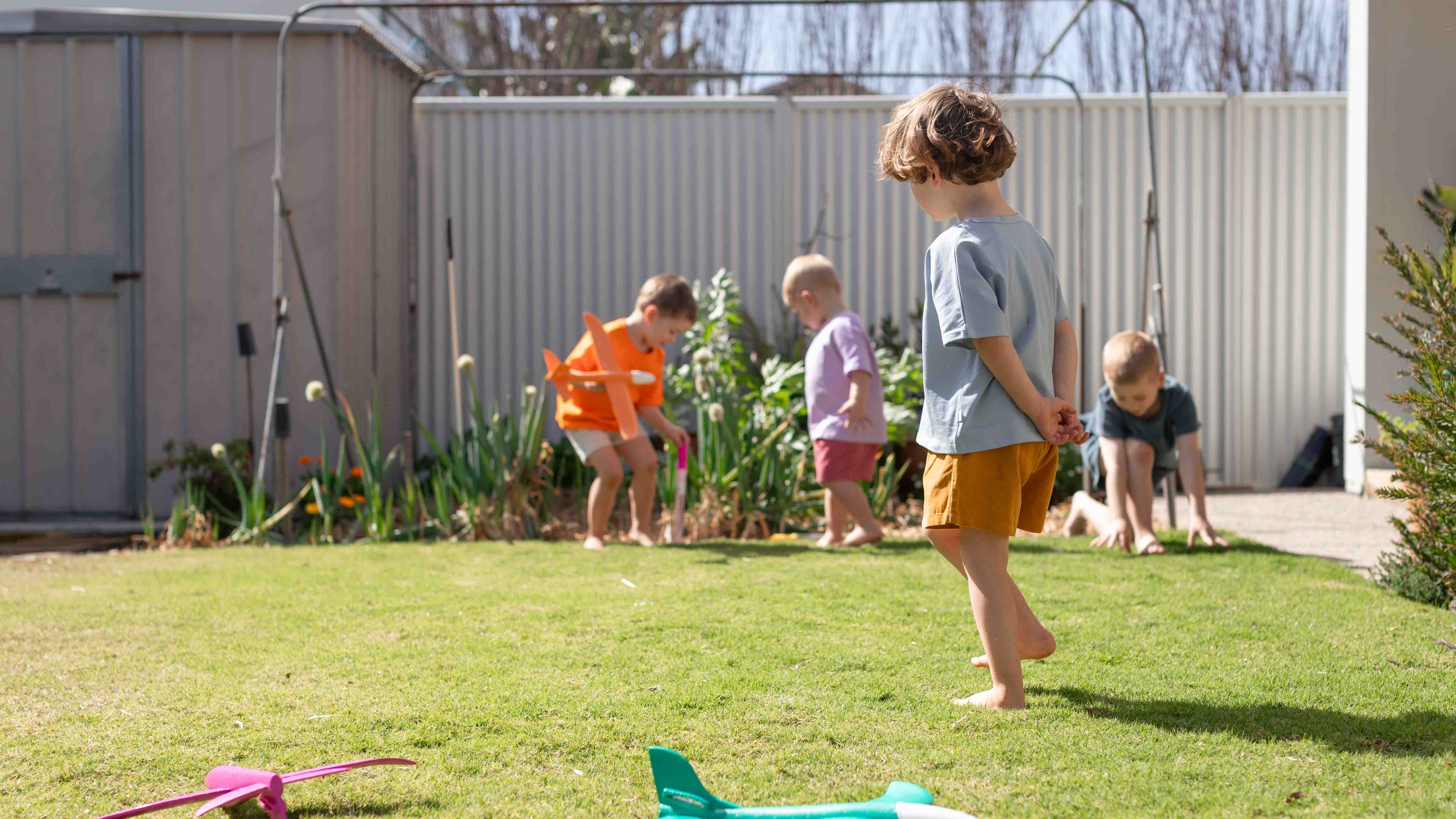 Young kid in a blue t-shirt and yellow cord shorts in front of three other kids in bright summer clothing