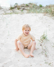 Child sitting on a sandy beach with grass and sand dunes in the background