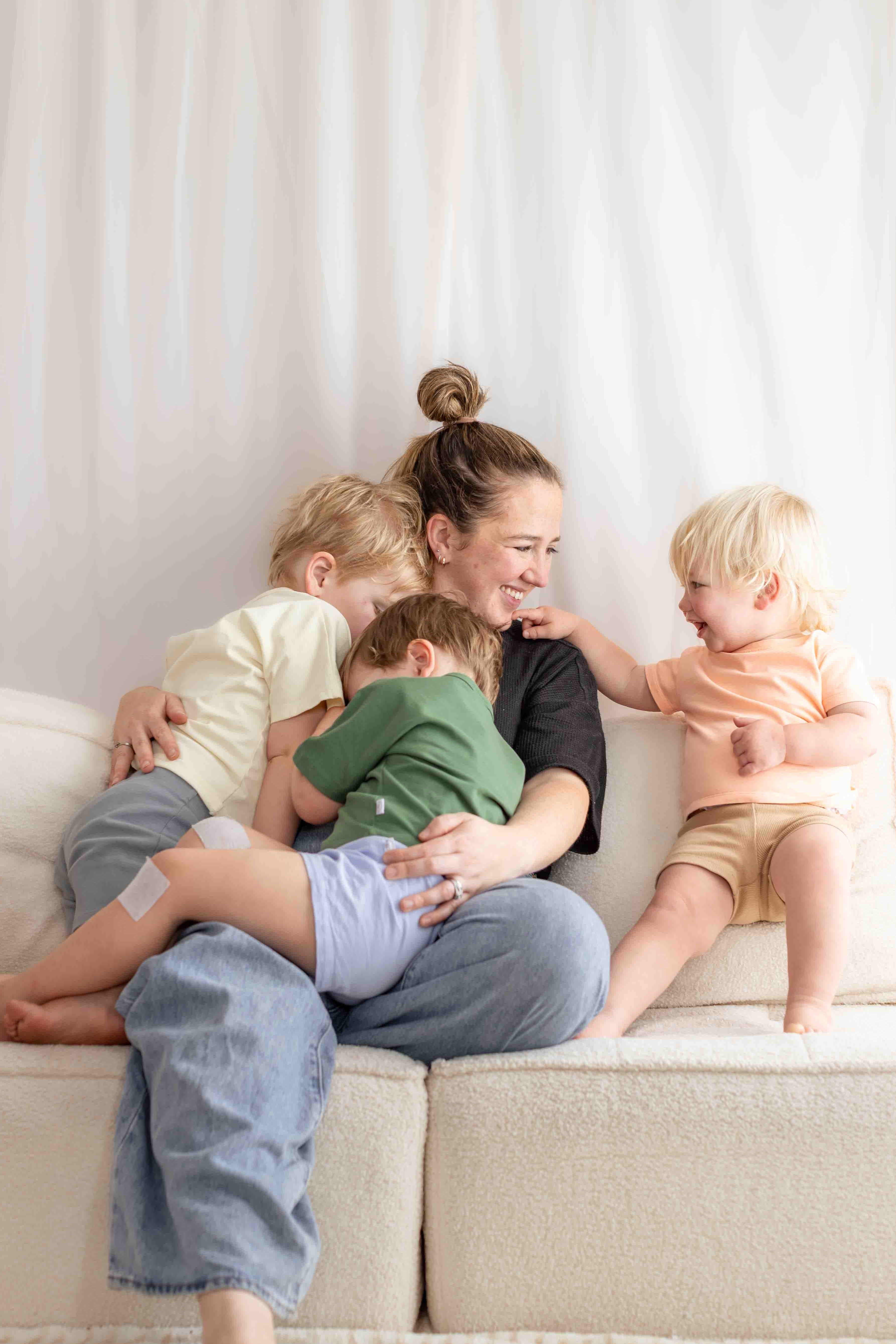 Woman sitting on a couch with three children, smiling and interacting.