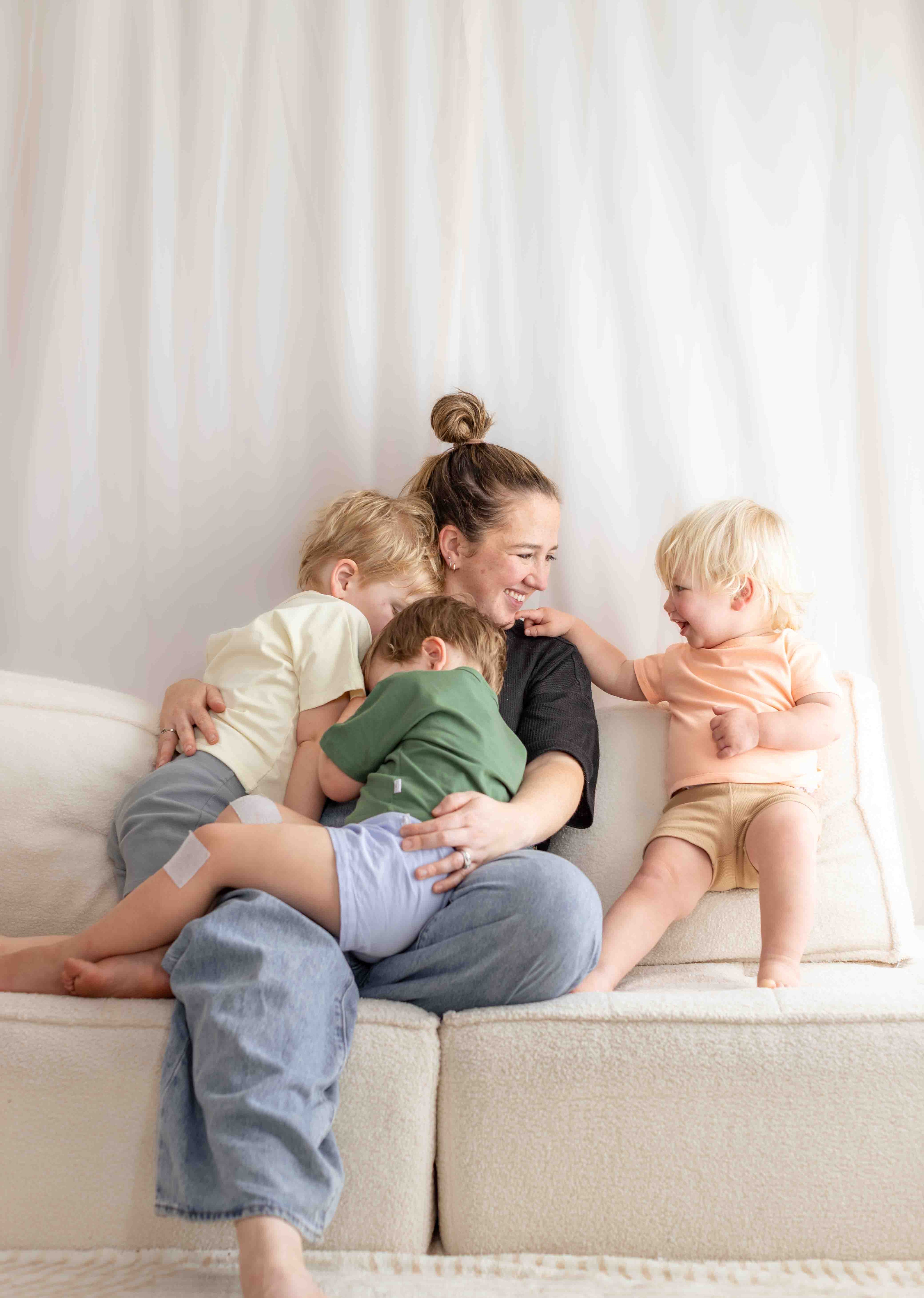 Woman sitting on a couch with three children, smiling and interacting.