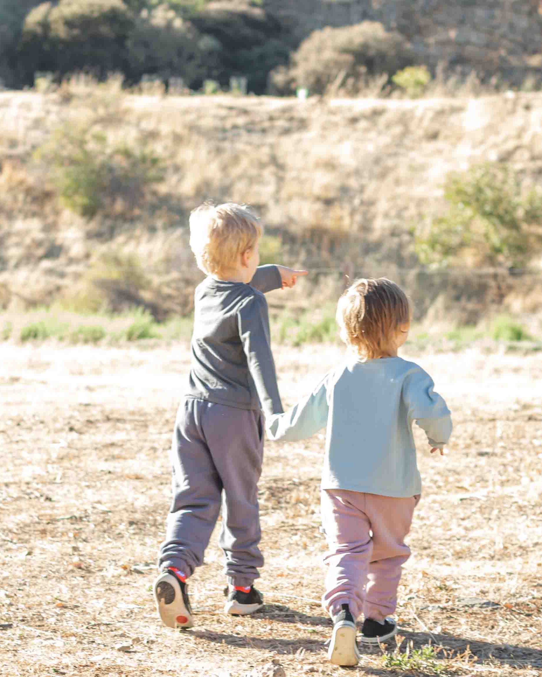 Two children walking together in a dry, open landscape with sparse vegetation.