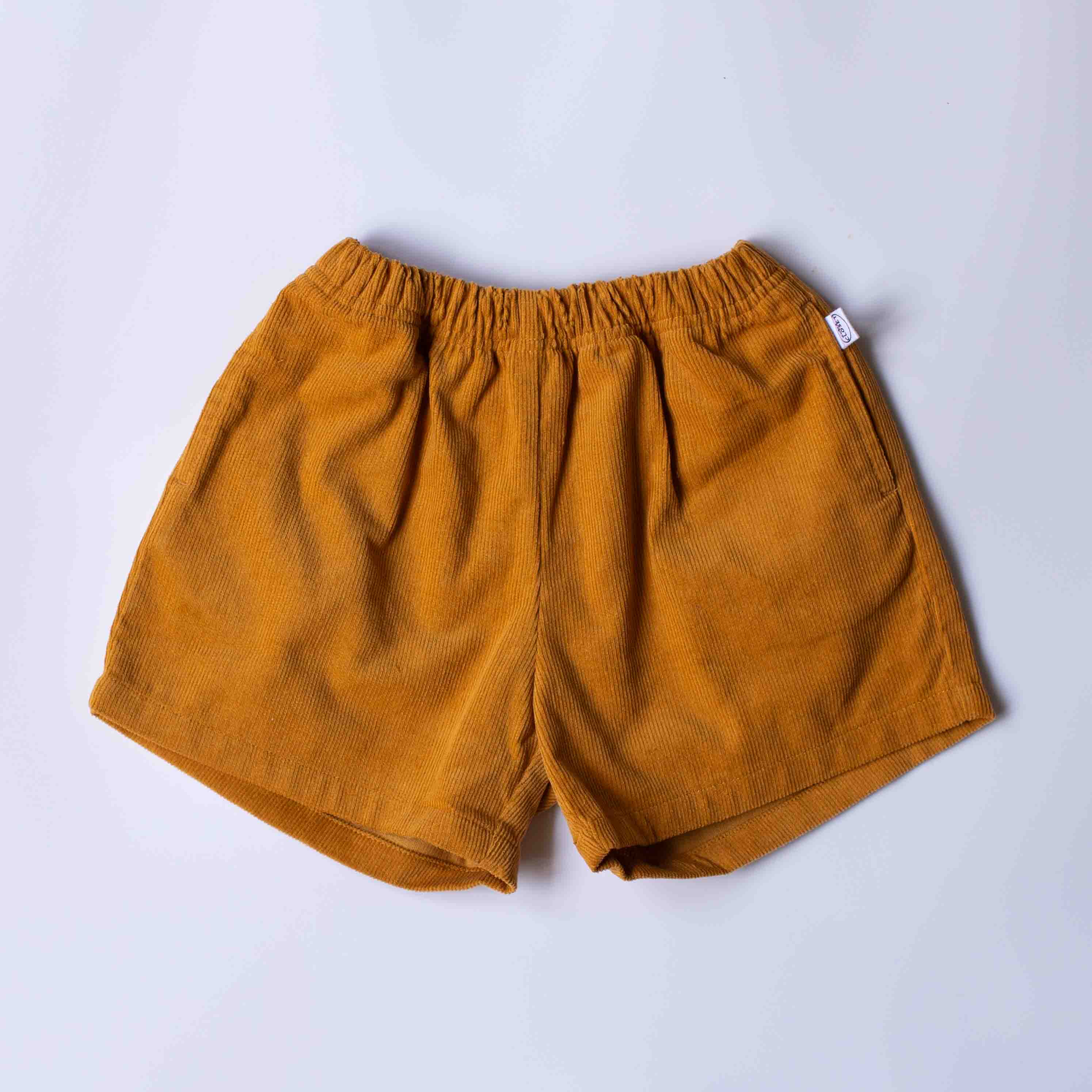 A pair of mustard yellow corduroy shorts with an elastic waistband, laid flat on a light gray background.