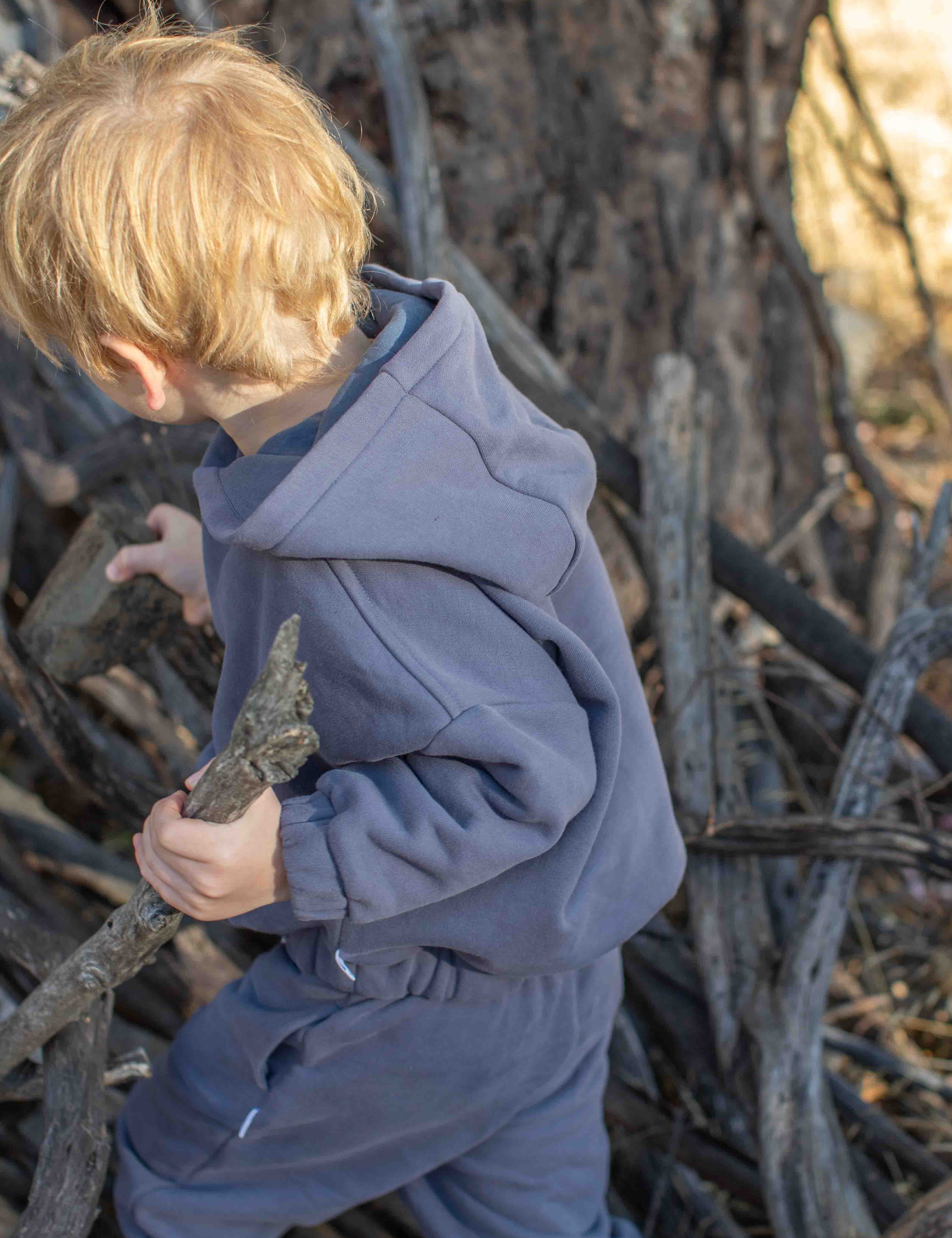 Child in a blue outfit standing among dry branches and twigs.