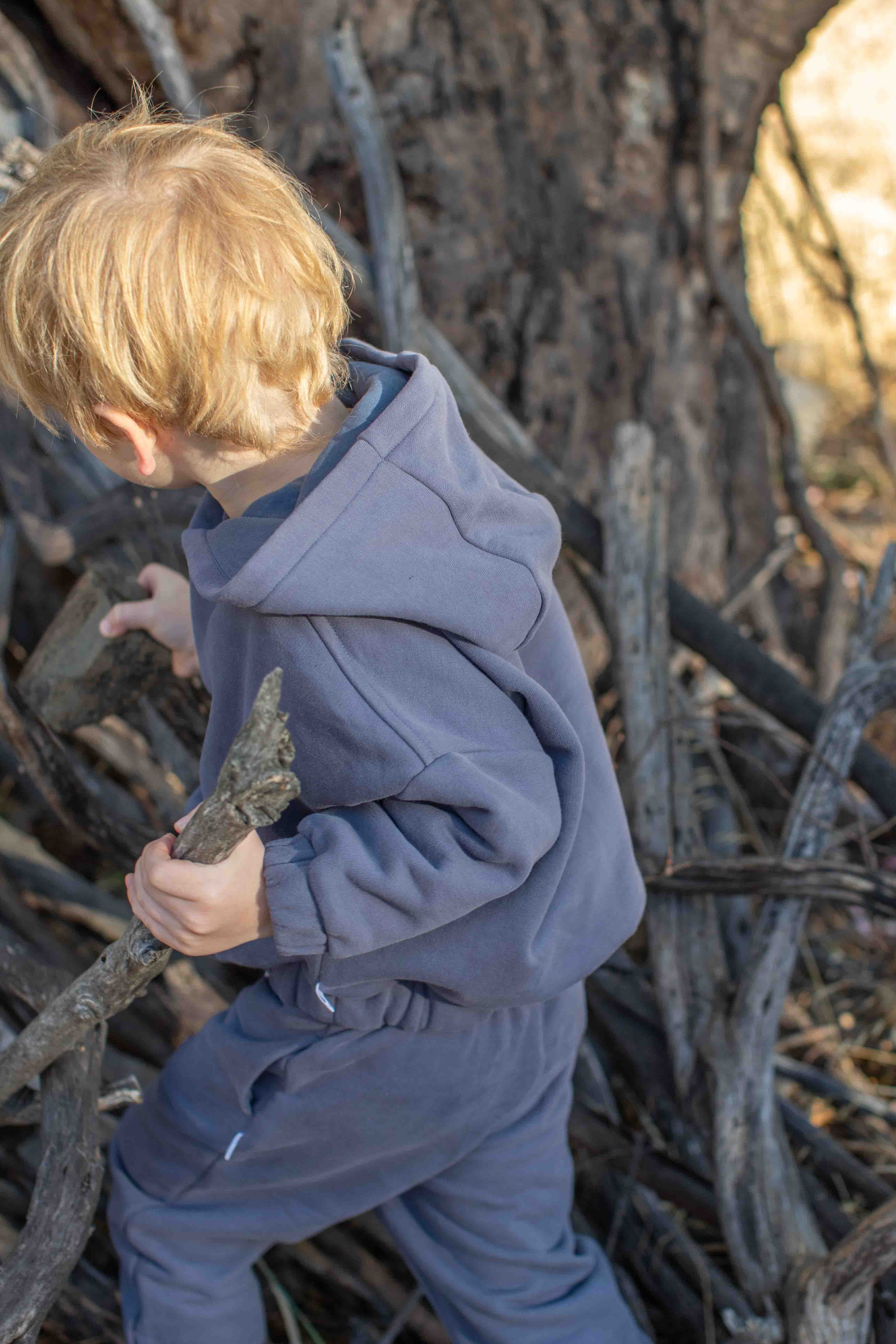 Child in a blue outfit standing among dry branches and twigs.