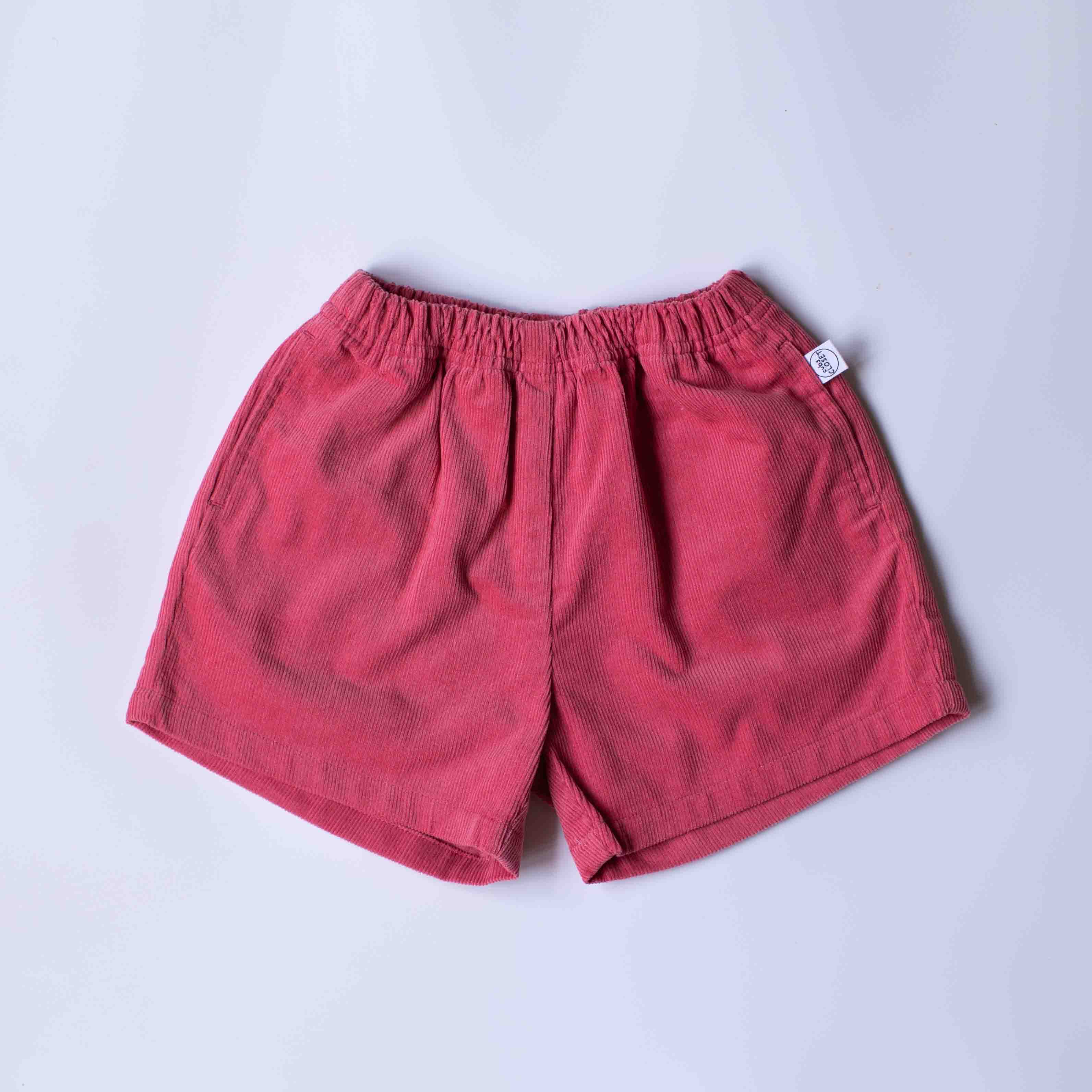 A pair of pink corduroy shorts with an elastic waistband, laid flat on a light gray background.