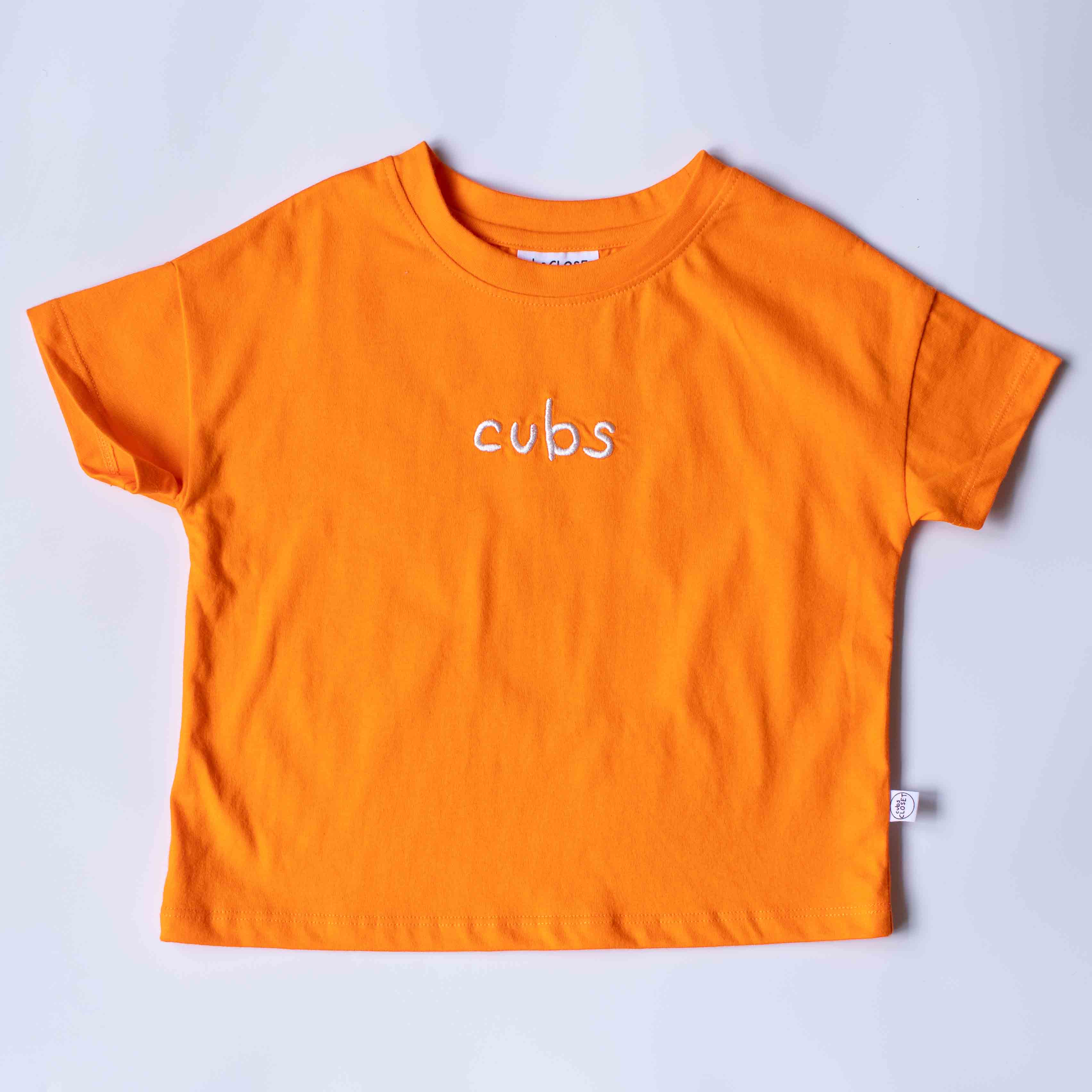 An orange short-sleeve t-shirt with the word 'cubs' embroidered in white across the chest, laid flat on a light gray background.