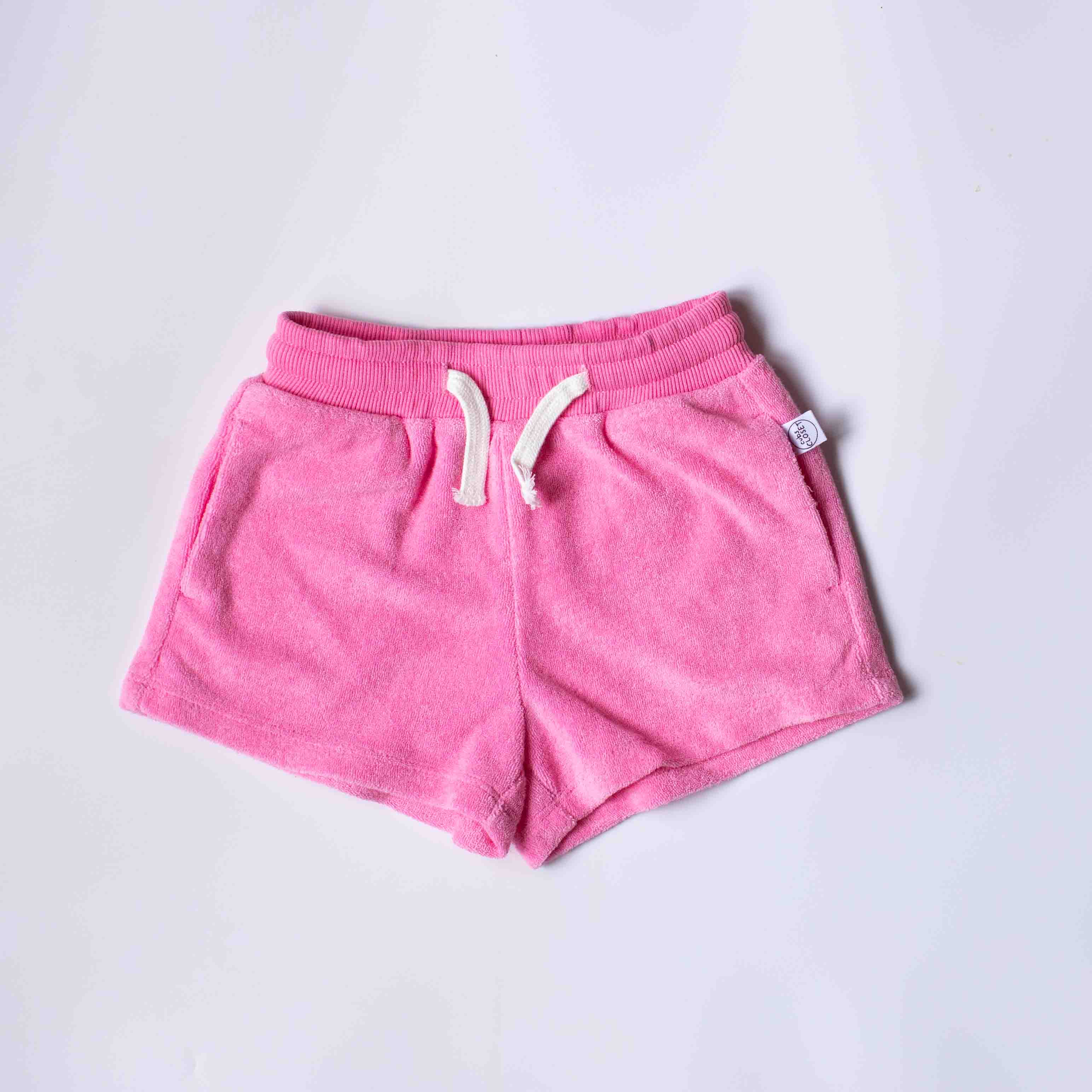 Pink fleece shorts with a white drawstring, laid flat on a light gray background.