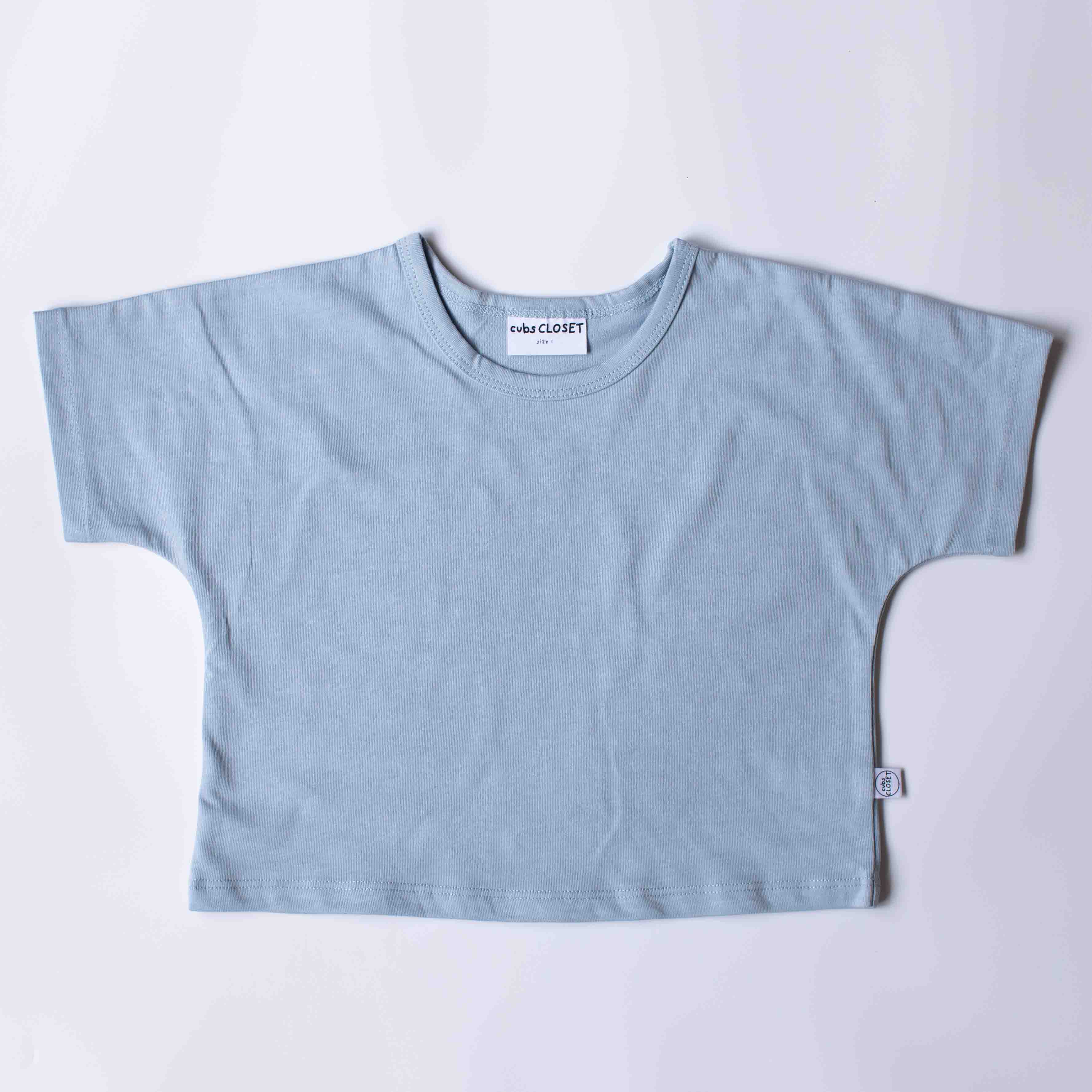A light blue short-sleeve crop top t-shirt laid flat on a light gray background. The shirt features a relaxed fit, short wide sleeves, and a crew neck with a visible 'miki CLOSET' brand label.